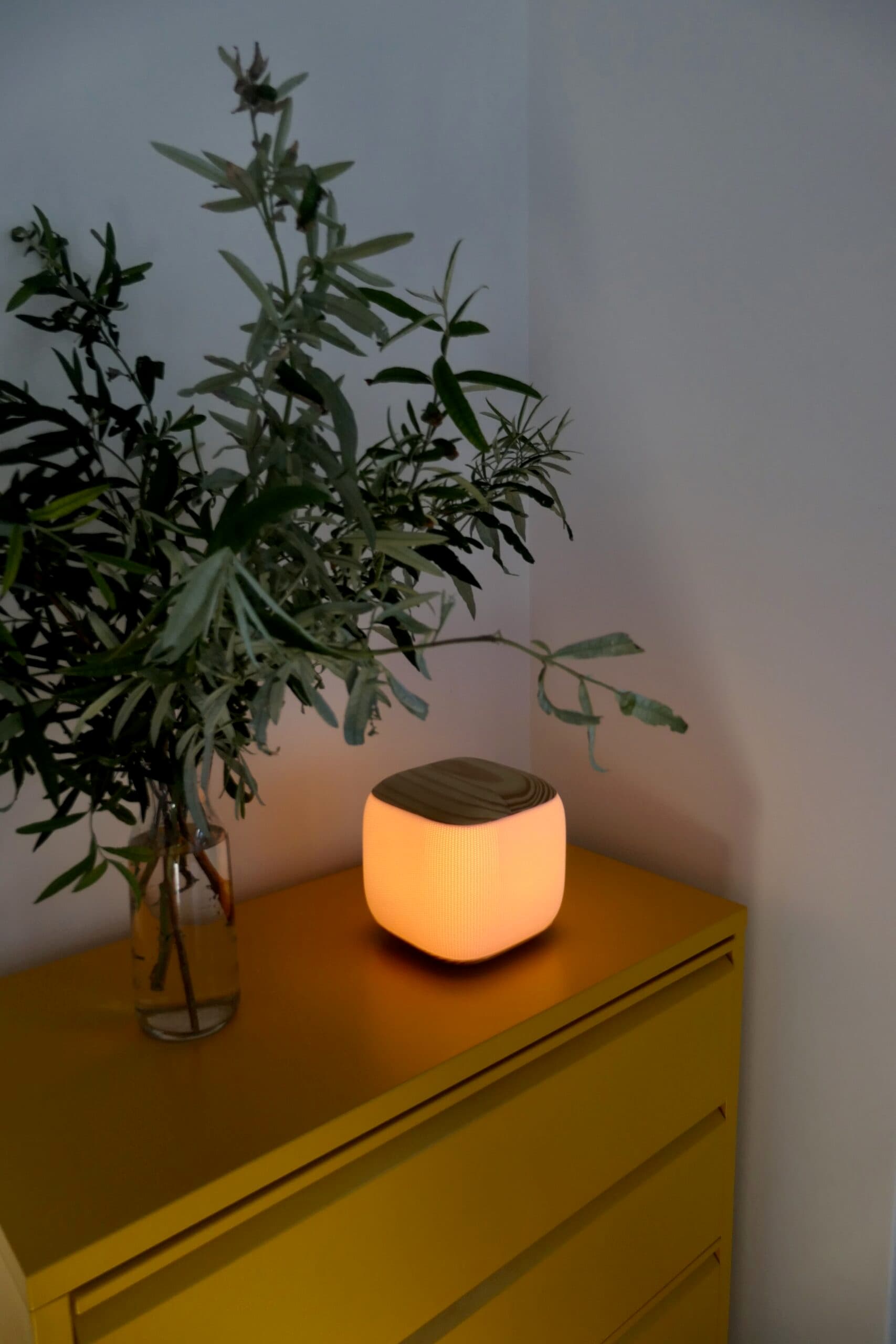 Jenny Lamp switched on in a corner, throwing warm light across a yellow cabinet